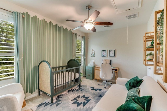 bedroom with carpet floors, visible vents, attic access, a nursery area, and a ceiling fan