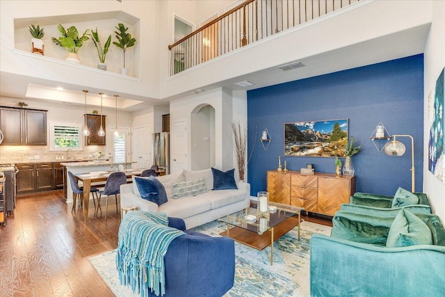living room featuring visible vents, a high ceiling, arched walkways, and wood finished floors