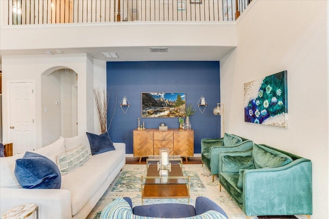 living room with arched walkways, a high ceiling, wood finished floors, and visible vents