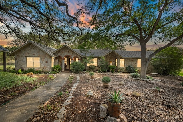 ranch-style home featuring a standing seam roof, stone siding, and metal roof