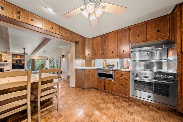 kitchen featuring a ceiling fan, appliances with stainless steel finishes, brown cabinets, open floor plan, and under cabinet range hood