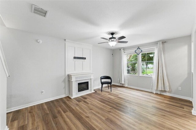 unfurnished room featuring ceiling fan, a glass covered fireplace, baseboards, wood finished floors, and visible vents