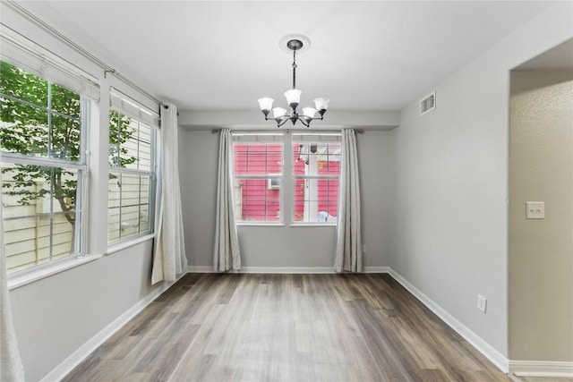 unfurnished dining area featuring baseboards, visible vents, wood finished floors, and an inviting chandelier