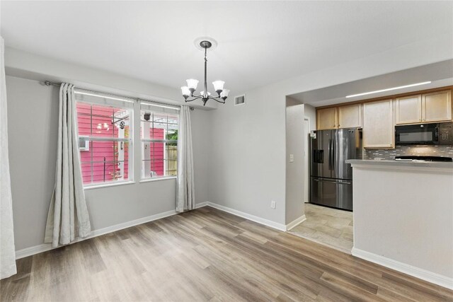 kitchen with visible vents, black microwave, stainless steel fridge, light wood-type flooring, and a chandelier