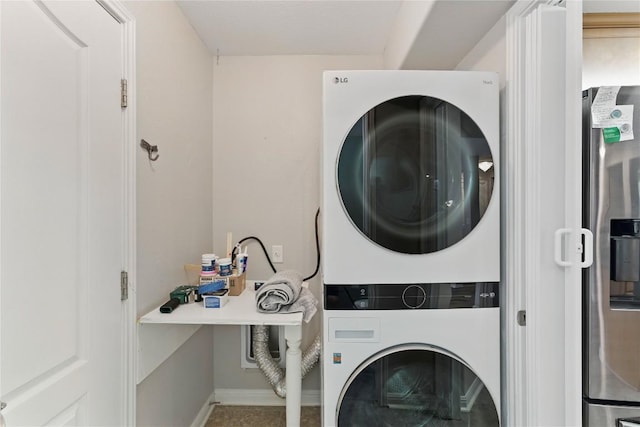 washroom with baseboards, stacked washer / drying machine, and laundry area