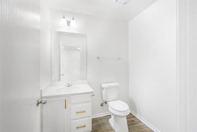 half bathroom with vanity, baseboards, toilet, and wood finished floors