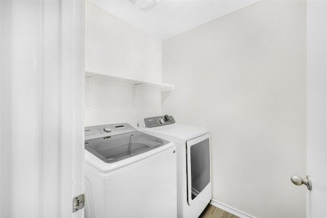 clothes washing area featuring baseboards, laundry area, wood finished floors, and washing machine and clothes dryer