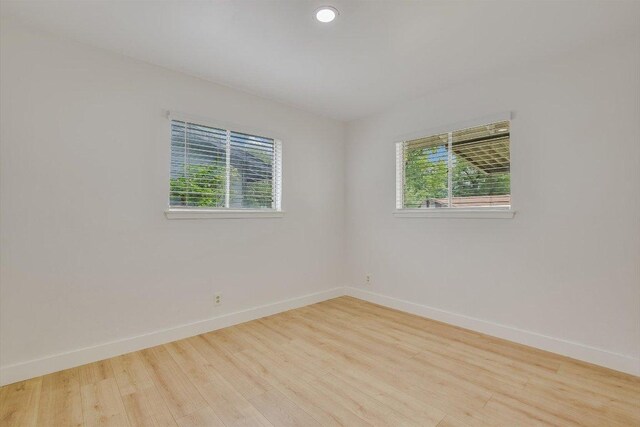 empty room with a healthy amount of sunlight, baseboards, and wood finished floors