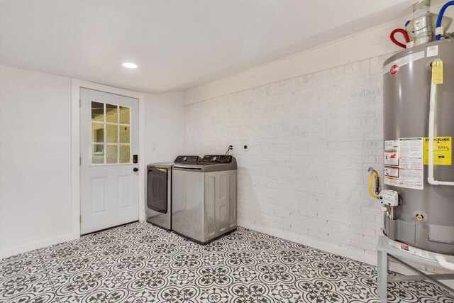 laundry room featuring laundry area, washing machine and dryer, brick wall, baseboards, and gas water heater