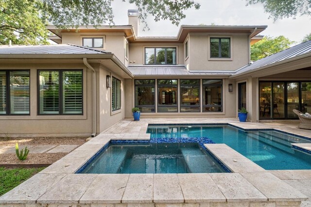 back of property featuring a chimney, a pool with connected hot tub, stucco siding, and metal roof