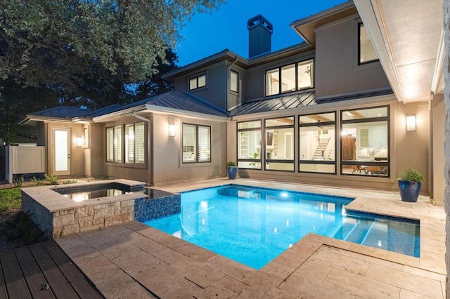 back of house at night with a standing seam roof, a chimney, metal roof, a patio area, and stucco siding