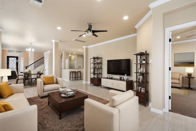 living area featuring visible vents, ornamental molding, baseboards, and ceiling fan with notable chandelier