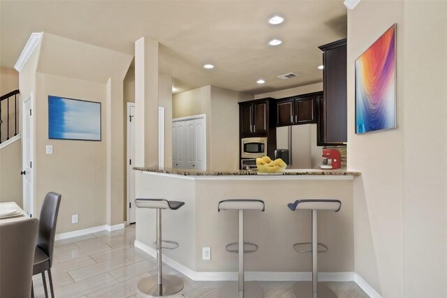 kitchen featuring visible vents, stone countertops, stainless steel microwave, freestanding refrigerator, and a breakfast bar