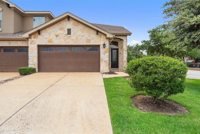 view of front facade with concrete driveway, a front yard, an attached garage, and stone siding