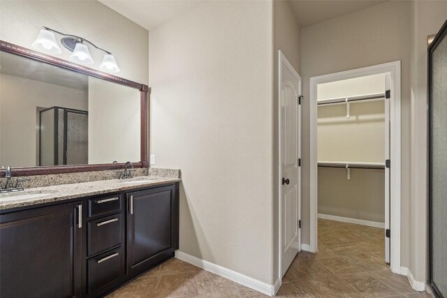 bathroom with double vanity, a spacious closet, a sink, and a stall shower
