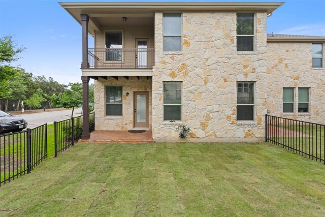 back of property with a fenced backyard, a yard, a balcony, and stone siding