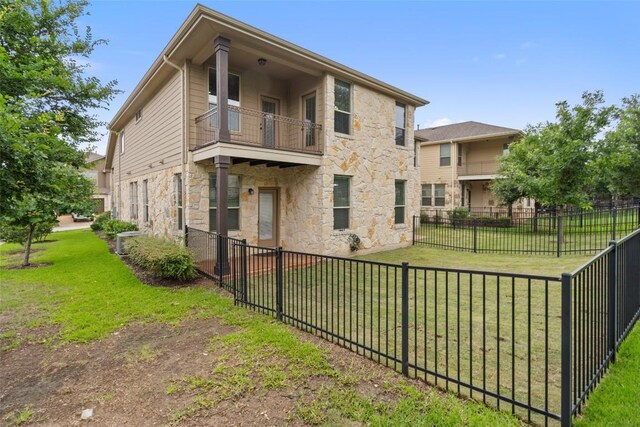 back of house with a yard, a fenced backyard, a balcony, and stone siding