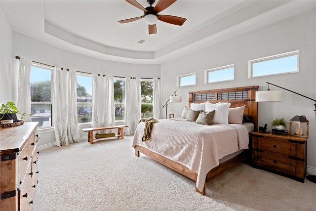carpeted bedroom featuring ceiling fan, visible vents, and a raised ceiling