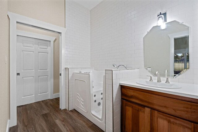 full bathroom featuring a jetted tub, tile walls, vanity, and wood finished floors