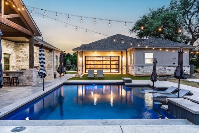 pool at dusk with outdoor dry bar, a patio area, and an outdoor pool