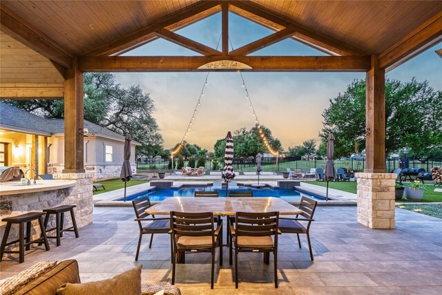 patio terrace at dusk featuring an outdoor bar, fence, a fenced in pool, and outdoor dining area