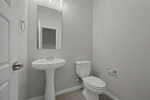 half bath featuring a sink, baseboards, toilet, and wood finished floors