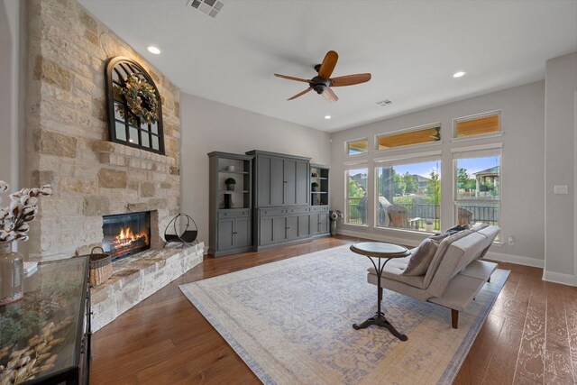 living room with ceiling fan, a stone fireplace, visible vents, wood finished floors, and baseboards