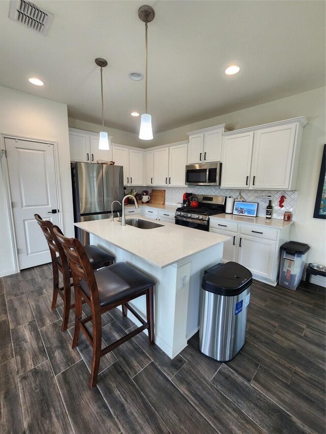 kitchen with a sink, light countertops, a kitchen breakfast bar, stainless steel appliances, and visible vents