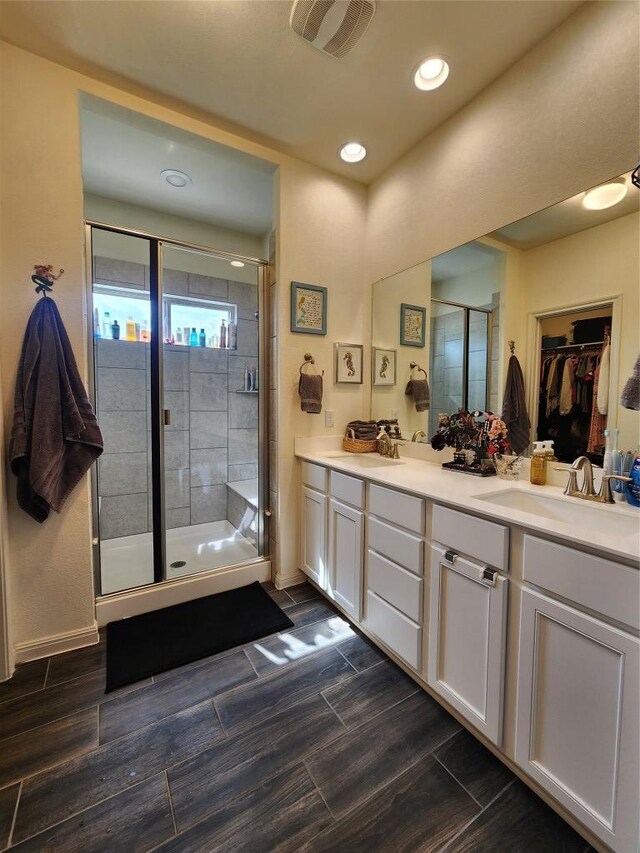 bathroom with double vanity, visible vents, a shower stall, a sink, and a spacious closet