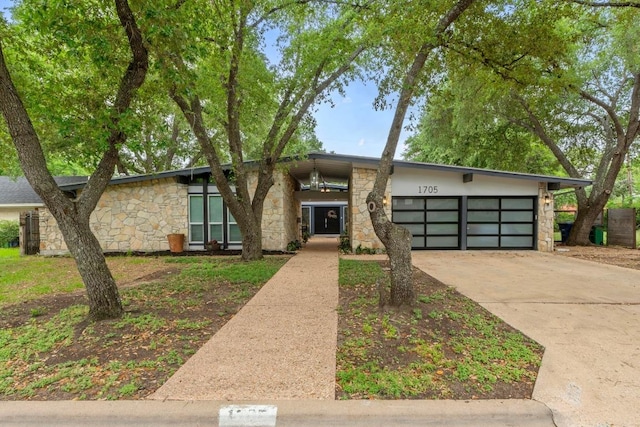 mid-century inspired home featuring concrete driveway, stone siding, and a garage