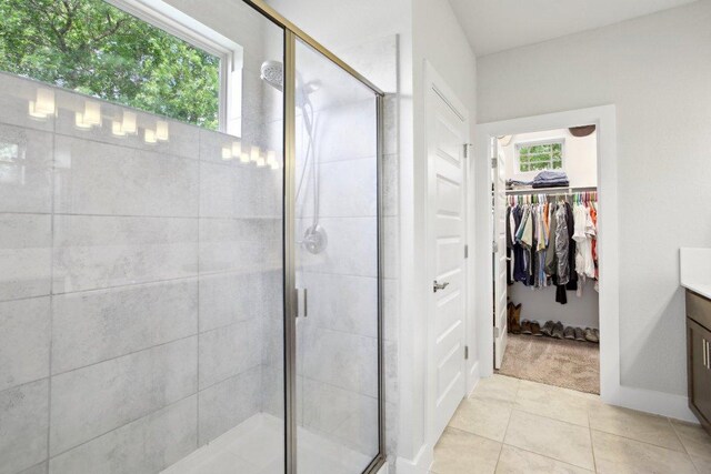 bathroom with a walk in closet, a shower stall, vanity, baseboards, and tile patterned floors