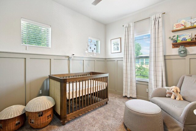 carpeted bedroom with a decorative wall, a nursery area, and a wainscoted wall