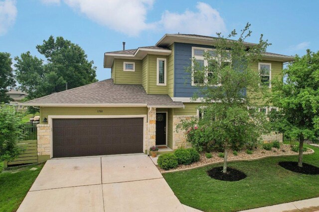 view of front facade with a garage, a front yard, stone siding, a shingled roof, and driveway