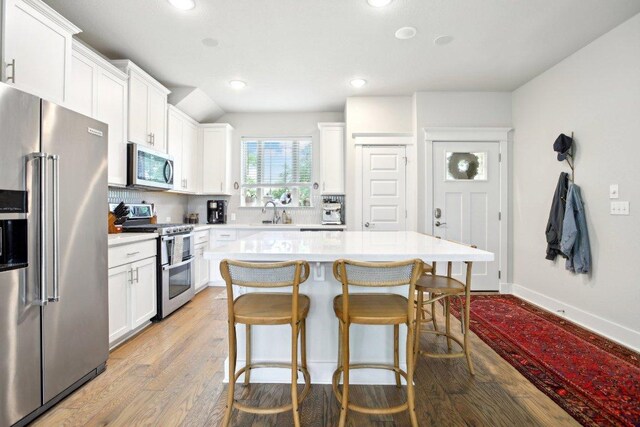 kitchen featuring light countertops, stainless steel appliances, white cabinetry, and a kitchen breakfast bar