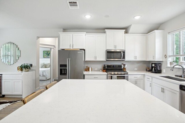 kitchen featuring backsplash, visible vents, a sink, stainless steel appliances, and white cabinetry