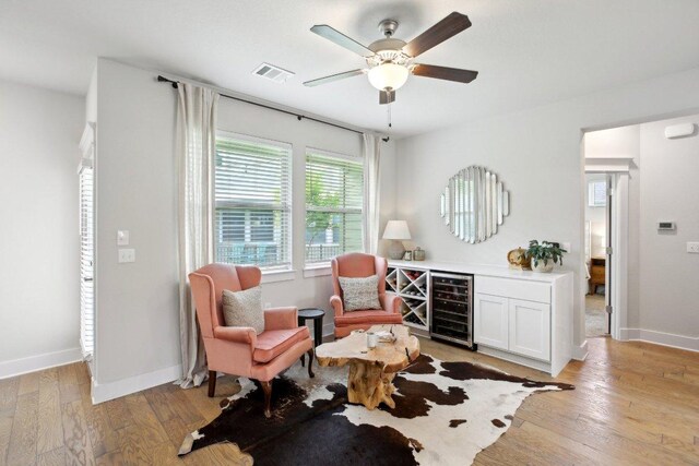 sitting room with ceiling fan, light wood finished floors, beverage cooler, baseboards, and visible vents