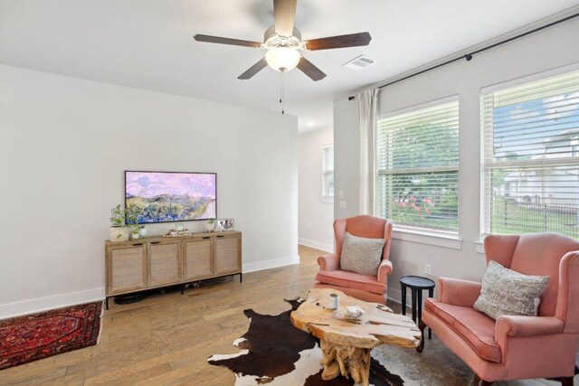 living area with baseboards, ceiling fan, wood finished floors, and visible vents