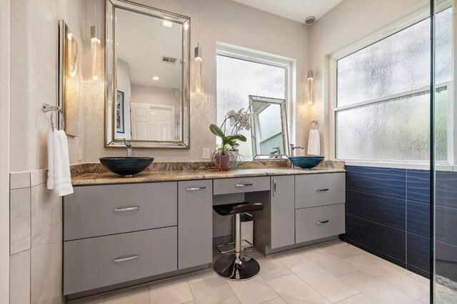 bathroom featuring a sink, visible vents, double vanity, and a healthy amount of sunlight