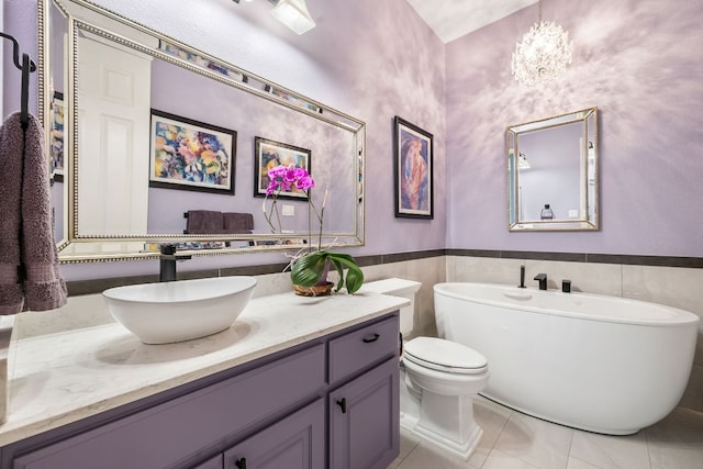 bathroom featuring a freestanding bath, tile patterned flooring, vanity, toilet, and a wainscoted wall