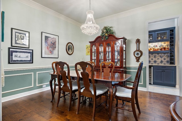 dining area with crown molding, wood finished floors, wine cooler, a bar, and an inviting chandelier