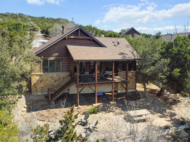 rear view of property featuring stairway, roof with shingles, stone siding, and a deck