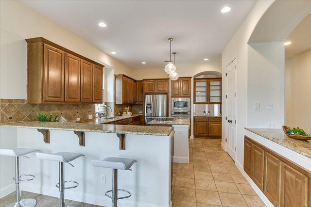 kitchen with a kitchen breakfast bar, appliances with stainless steel finishes, tasteful backsplash, a sink, and light stone counters