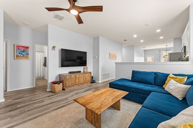 living area featuring visible vents, a ceiling fan, light wood finished floors, and baseboards