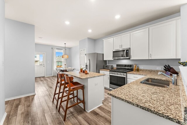 kitchen featuring a kitchen island, appliances with stainless steel finishes, a sink, and light wood finished floors