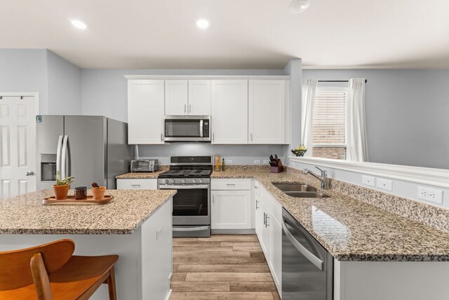 kitchen with a sink, light wood-style flooring, appliances with stainless steel finishes, and white cabinetry