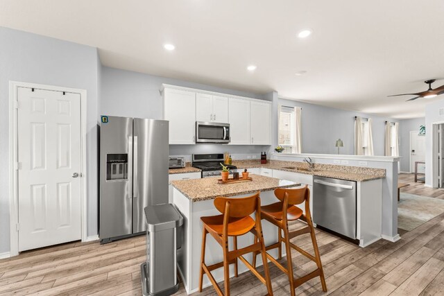 kitchen featuring a peninsula, light wood-type flooring, a center island, white cabinetry, and appliances with stainless steel finishes