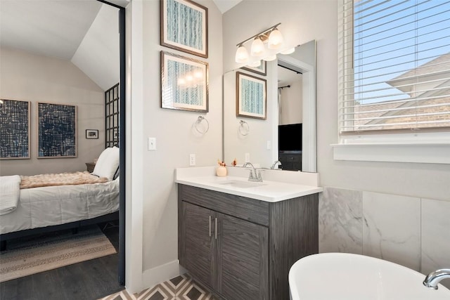 ensuite bathroom with a freestanding tub, vaulted ceiling, vanity, baseboards, and connected bathroom