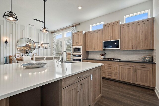 kitchen with pendant lighting, dark wood-type flooring, a sink, appliances with stainless steel finishes, and backsplash