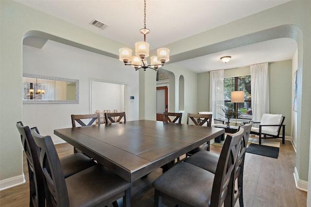 dining room featuring visible vents, arched walkways, wood finished floors, and an inviting chandelier