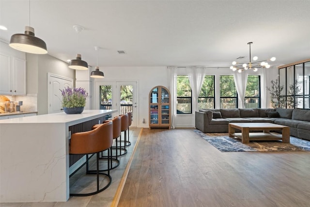 living area with a healthy amount of sunlight, visible vents, light wood-type flooring, and a notable chandelier